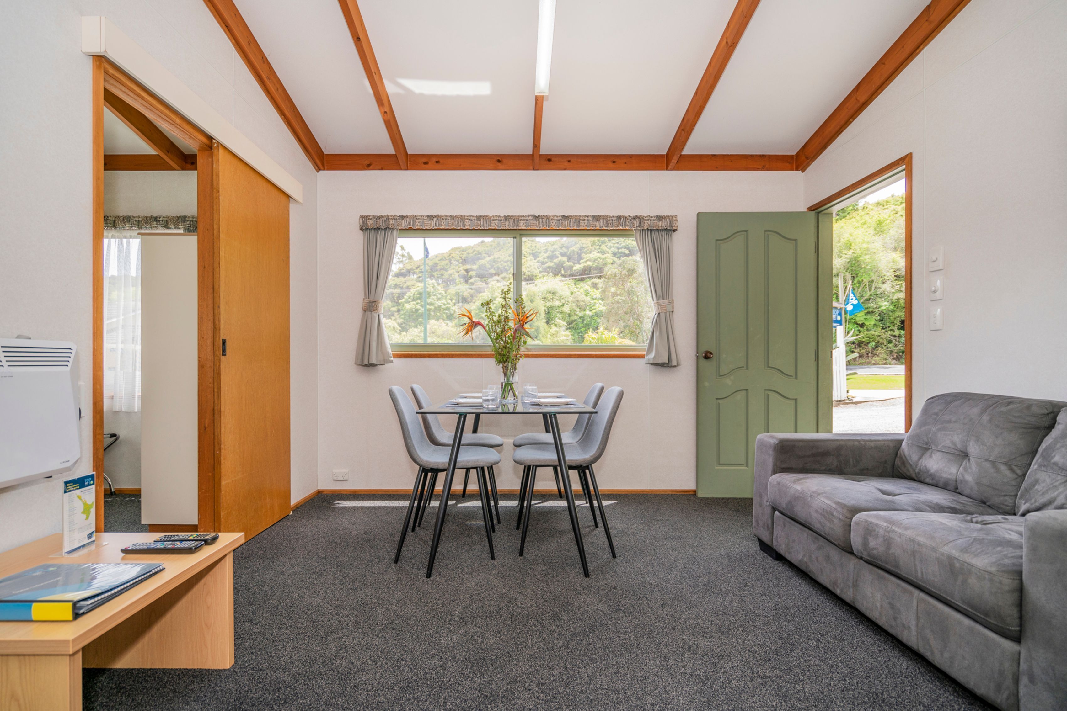 A room with a dining table, chairs, a sofa, a window with curtains, and a door.