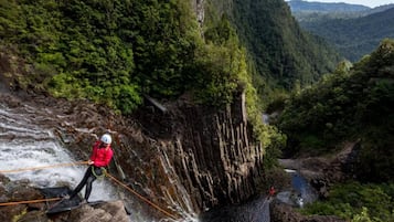 Une personne qui descend en rappel une falaise rocheuse, avec une rivière en contrebas.