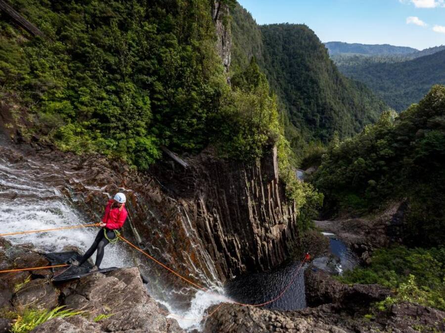 Une personne qui descend en rappel une falaise rocheuse, avec une rivière en contrebas.