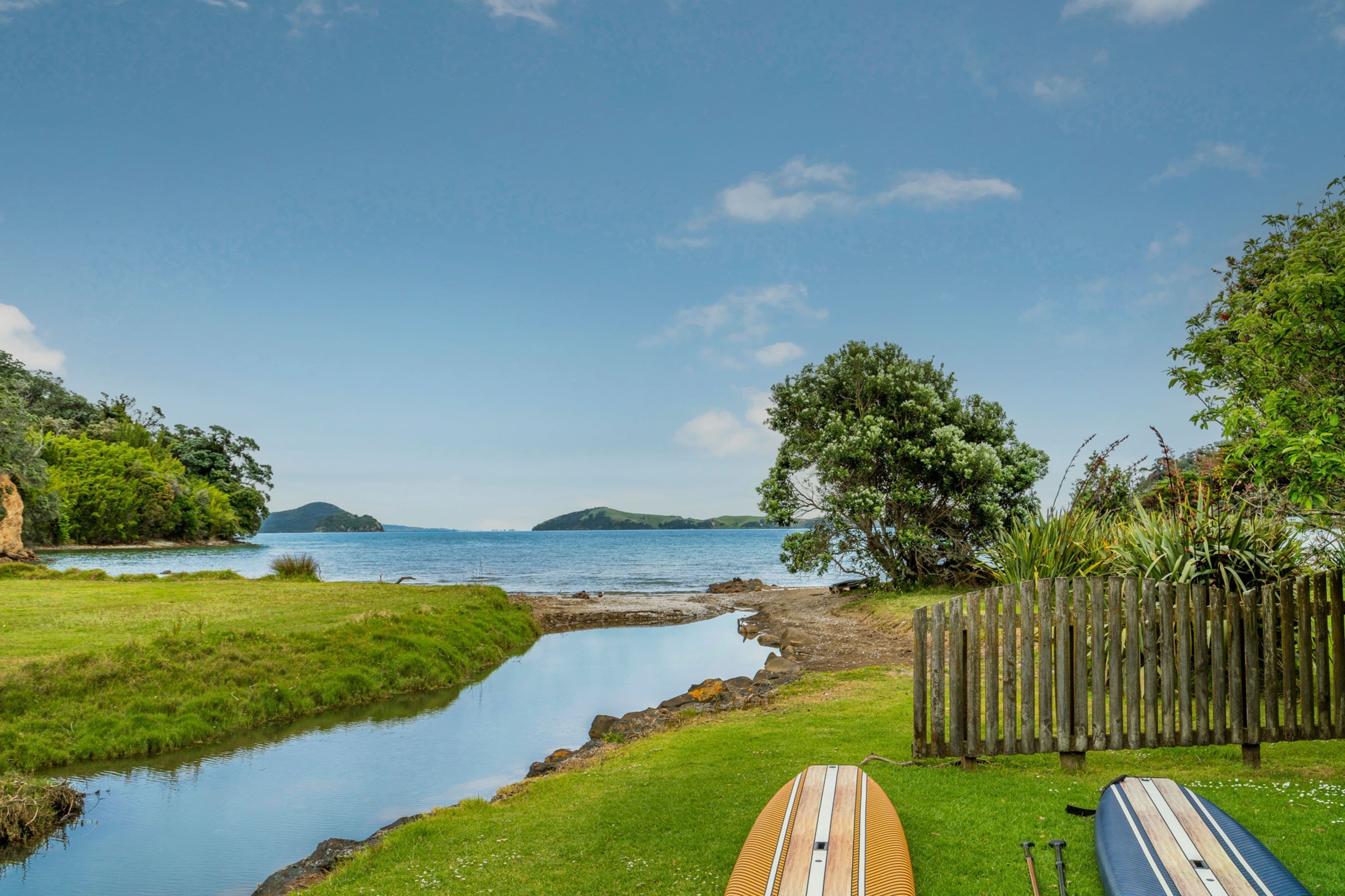 A riverside view with a wooden fence, paddleboards, and a calm water body.
