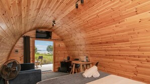 A cozy, wooden cabin room with a bed, a small table, a chair, and a fan. - Coromandel Shelly Beach TOP 10 Holiday Park (Coromandel)