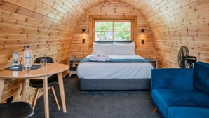 A cozy, wooden-paneled room with a bed, a blue sofa, a small table, and a fan. - Coromandel Shelly Beach TOP 10 Holiday Park (Coromandel)