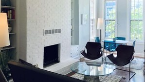A modern living room with a white brick fireplace, a glass coffee table, and black chairs.
