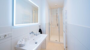 Une salle de bain moderne avec un lavabo blanc, un miroir et une douche en verre.