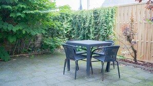 Une terrasse avec une table et des chaises, entourée d’une clôture en bois et de verdure.
