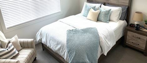 A bedroom with a bed, bedside table, lamp, and chair.