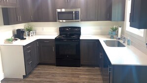 A modern kitchen with dark cabinets, a stainless steel microwave, a black stove, and a sink. - ★Home away from Home ★ (Tremonton)