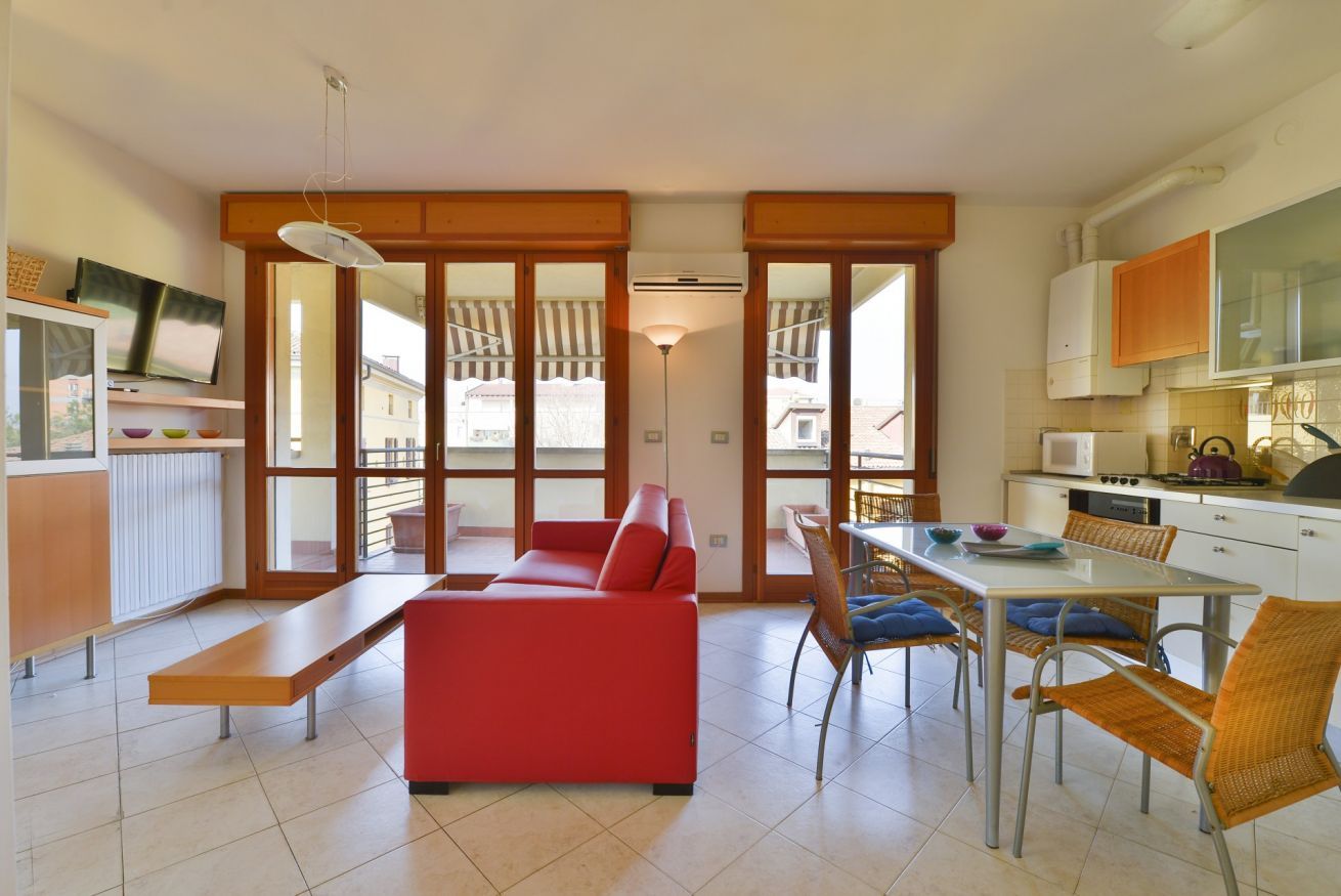 A modern kitchen with a dining area, featuring a red sofa, a dining table, and chairs.