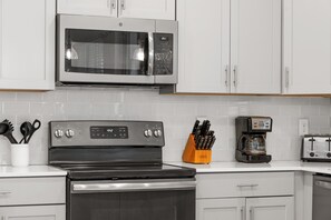 Eine Küche mit weißen Schränken, einer Edelstahl-Mikrowelle, einem schwarzen Backofen und einer Kaffeemaschine.