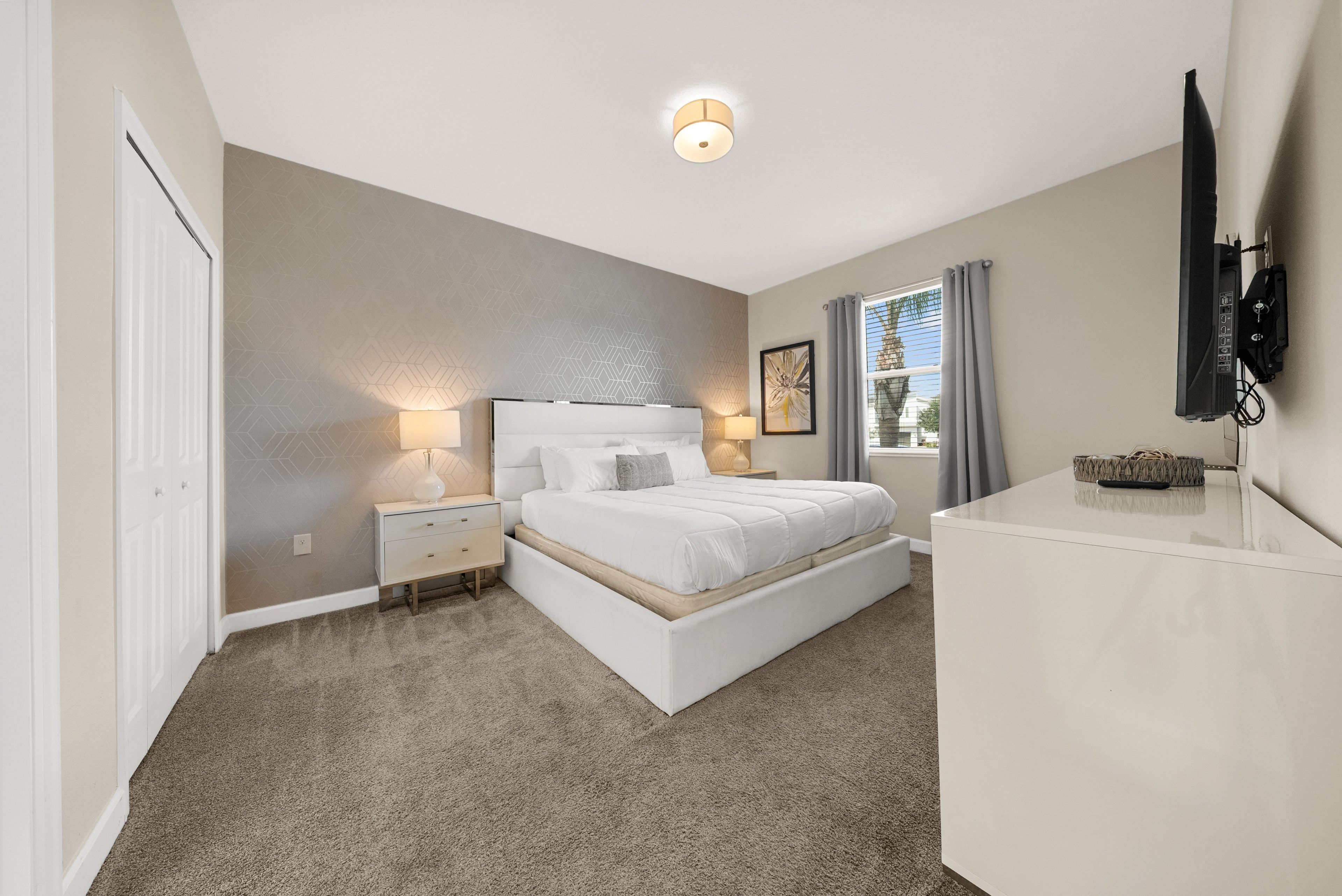 A bedroom with a bed, bedside tables, a TV, and a window with curtains.