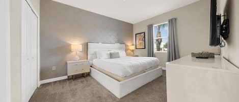 A bedroom with a bed, bedside tables, a TV, and a window with curtains.