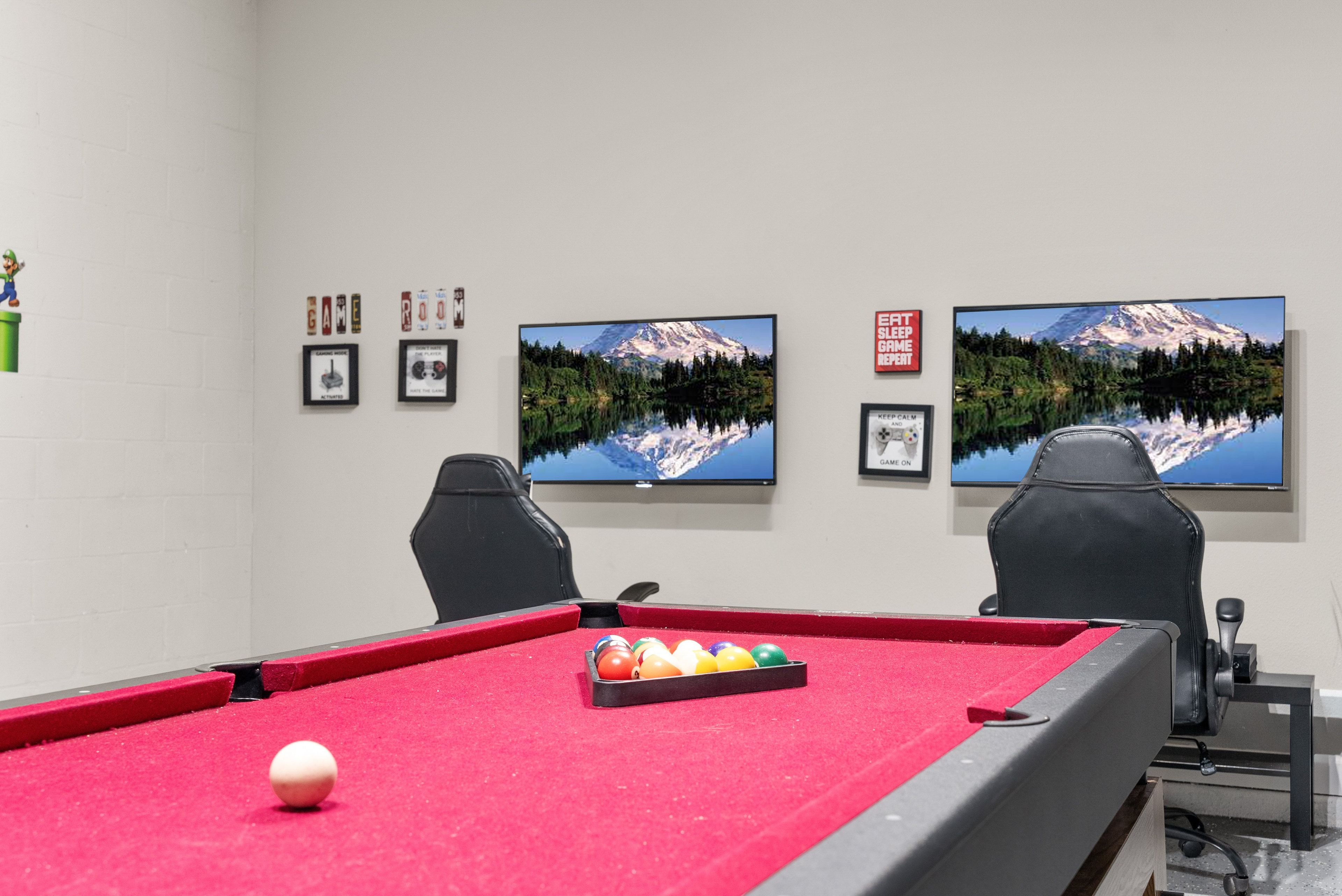 A pool table with balls, two chairs, and framed pictures on the wall.