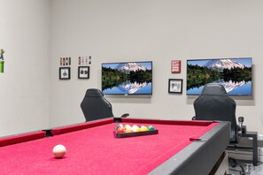 Ein Billardtisch mit Kugeln, zwei Stühle und gerahmte Bilder an der Wand.