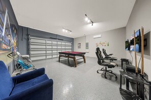 Une pièce comprenant une table de billard, des chaises, un canapé bleu, une table de jeux et un mur orné d’une fresque.