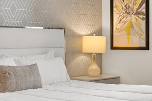 Ein ordentlich bezogenes Bett mit weißen Leinentüchern, einem strukturierten Kopfkissen und einem Nachttisch mit Lampe.