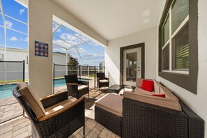 Ein überdachter Patio-Bereich mit Korbmöbeln, einem Pool und einer Tür zum Innenbereich.
