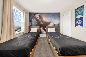 A bedroom with two single beds, a large poster on the wall, and a window with blinds.