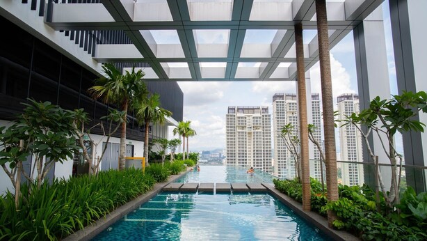 A modern indoor swimming pool with a view of high-rise buildings, surrounded by greenery and a covered walkway. - Aurora Pavilion Bukit Jalil by Ody Suites (Kuala Lumpur)