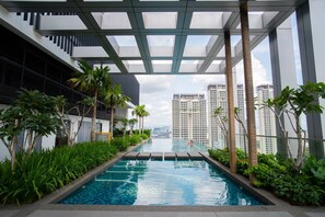 A modern indoor swimming pool with a view of high-rise buildings, surrounded by greenery and a covered walkway. - Aurora Pavilion Bukit Jalil by Ody Suites (Kuala Lumpur)