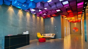 A modern lobby with a reception desk, a yellow chair, a red ottoman, and a grey sofa. - Aurora Pavilion Bukit Jalil by Ody Suites (Kuala Lumpur)