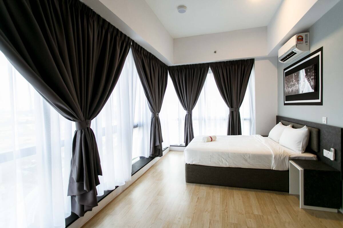 A modern hotel room with a large bed, a bedside table, a nightstand, and a window with curtains.