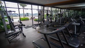 A gym with treadmills, weight machines, and a view of a cityscape through large windows. - Aurora Pavilion Bukit Jalil by Ody Suites (Kuala Lumpur)