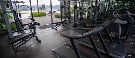 A gym with treadmills, weight machines, and a view of a cityscape through large windows.