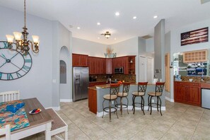 A spacious kitchen with a central island, wooden cabinets, and a clock on the wall. - Bailey Rose - Luxury Home Sailboat Access Canal (Cape Coral)