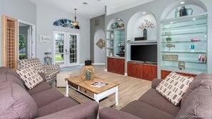 A spacious living room with a ceiling fan, a TV, and a glass display cabinet.