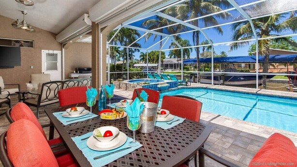 A dining area with a pool view, outdoor seating, and a large window overlooking palm trees.
