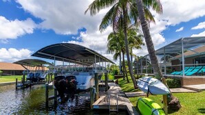 A marina with boats docked, a covered boat launch ramp, and a pool area with umbrellas.