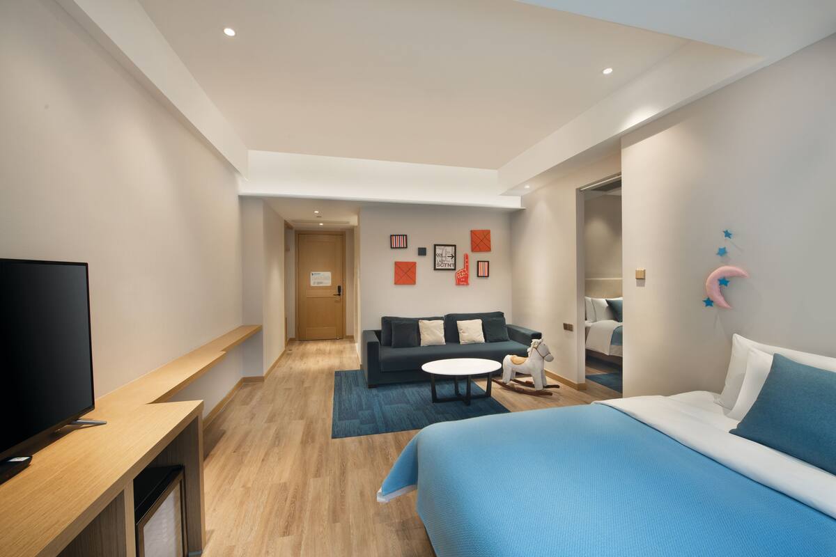 A modern hotel room with a large bed, a flat-screen TV, a sofa, and a small table.