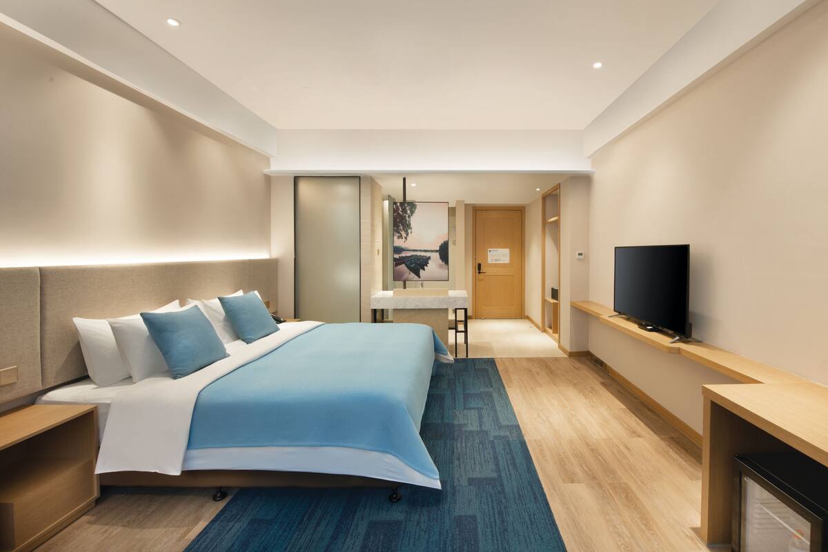 A modern hotel room with a large bed, a flat-screen TV, a desk, and a bathroom visible through an open door.