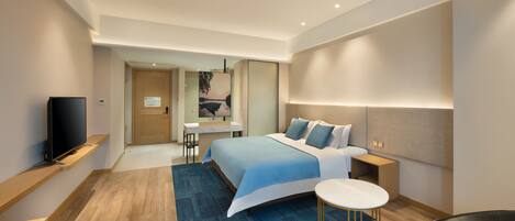 A modern hotel room with a large bed, a desk, and a TV.