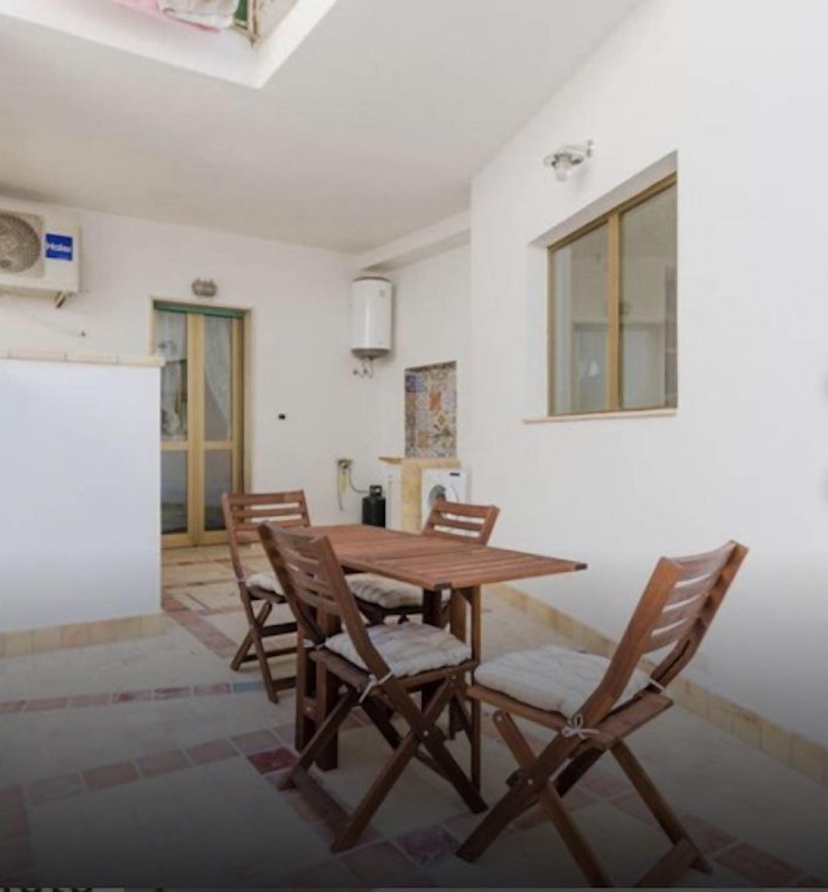 Un coin repas avec une table et des chaises en bois, un sol carrelé et une fenêtre.