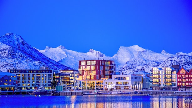 A waterfront hotel with multiple buildings, a dock with boats, and snow-covered mountains in the background. - Nordis Apartments (Vagan)