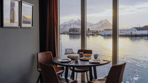 A dining table with chairs, a window with a view of mountains and water, and framed pictures on the wall. - Nordis Apartments (Vagan)