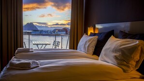 A hotel room with a bed, pillows, and a view of a dock and mountains. - Nordis Apartments (Vagan)