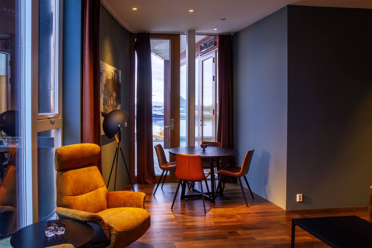 A modern room with a large window, a dining table with chairs, a sofa, and a floor lamp.