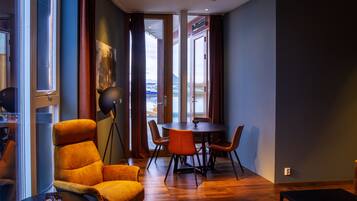 A modern room with a large window, a dining table with chairs, a sofa, and a floor lamp.