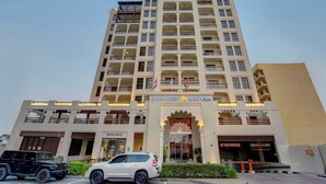 Un hôtel à plusieurs étages, doté de balcons, d’une entrée principale et d’un espace de stationnement pouvant accueillir deux voitures.