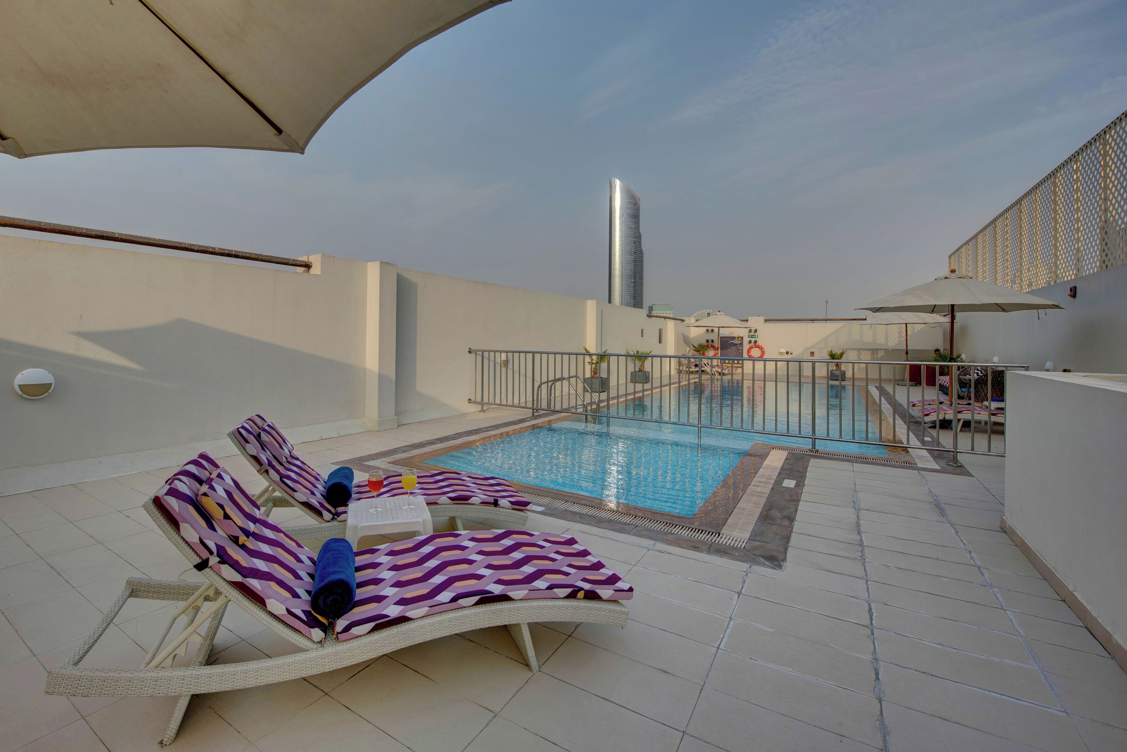 A rooftop pool area with lounge chairs and a view of a tall building in the background.