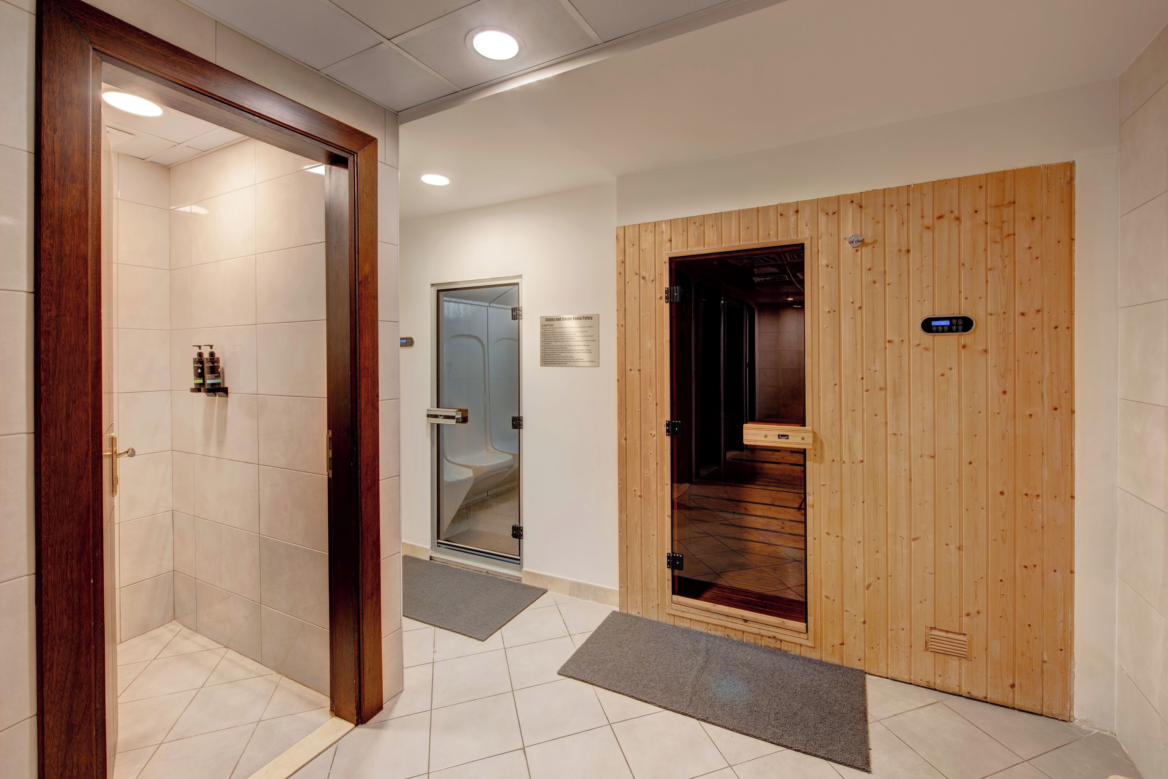 A hotel entrance with a wooden door, a glass shower room, and a tiled floor.