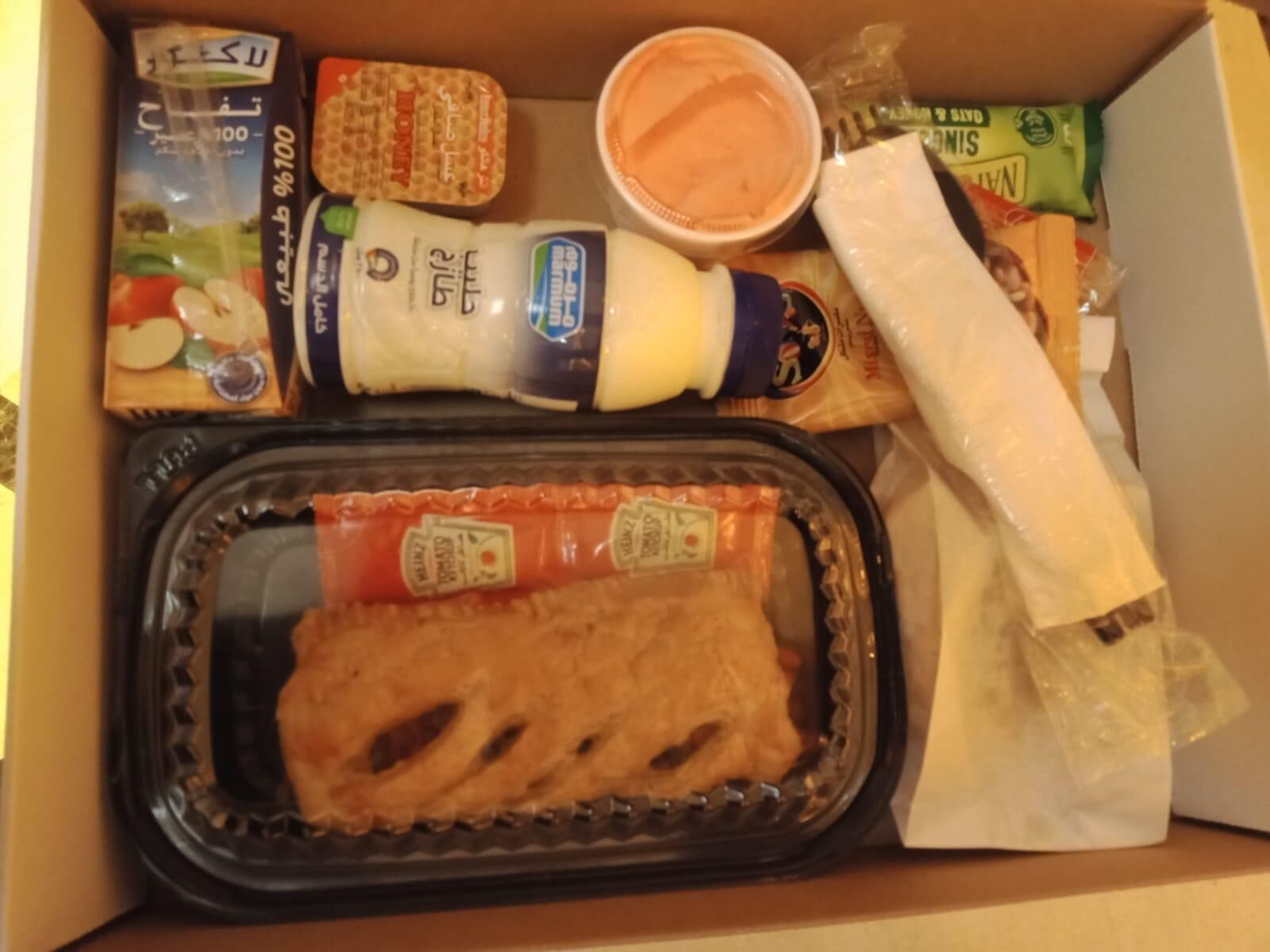 Une boîte repas contenant un sandwich, un récipient de sauce, une bouteille de vinaigrette et quelques collations.