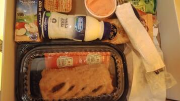 Une boîte repas contenant un sandwich, un récipient de sauce, une bouteille de vinaigrette et quelques collations.