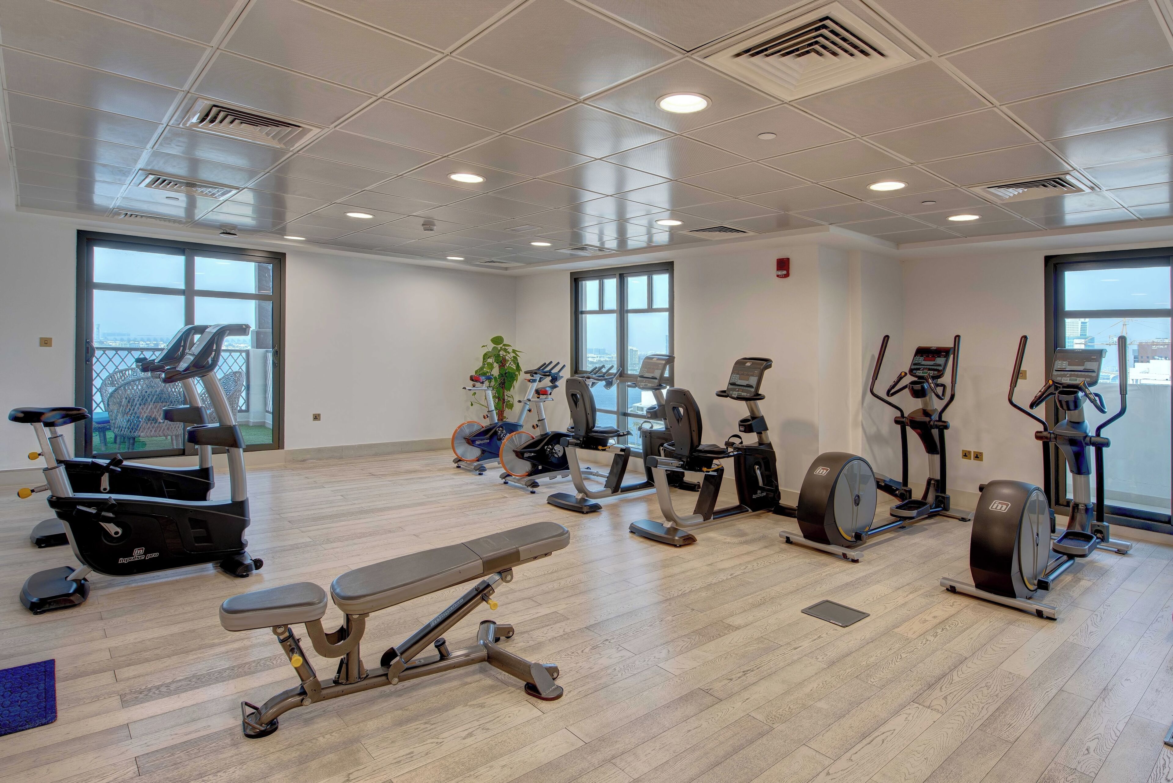 Una palestra con diverse attrezzature per esercizi, ampie finestre e vista sulla città.