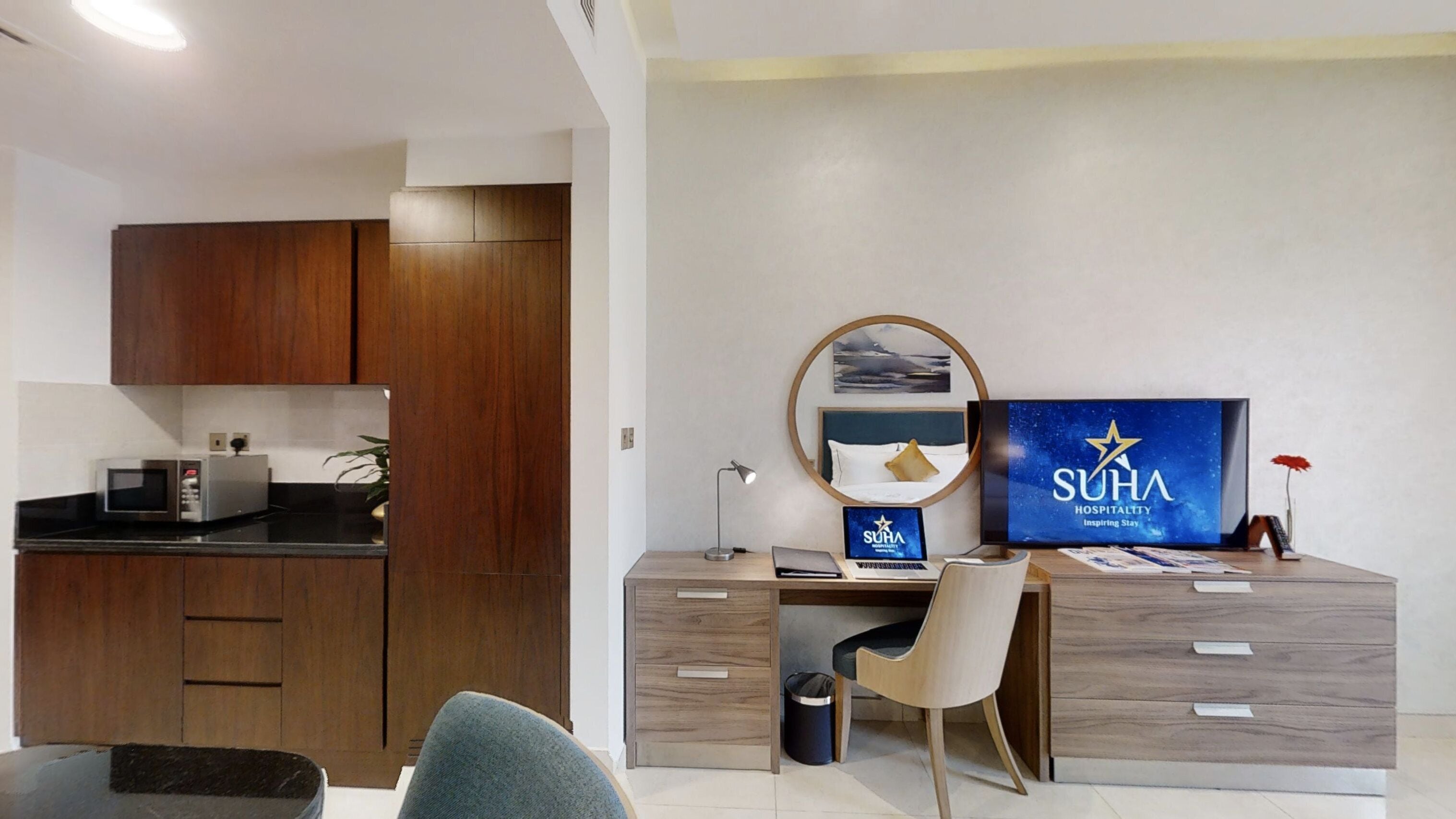 Habitació d'hotel moderna amb cuineta, escriptori amb ordinador, televisió i llit.