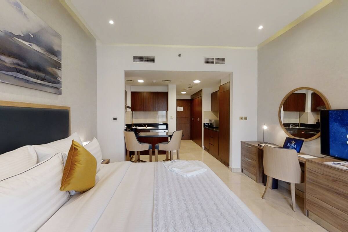Habitación de hotel con cama, escritorio, silla, televisor y área de cocina.