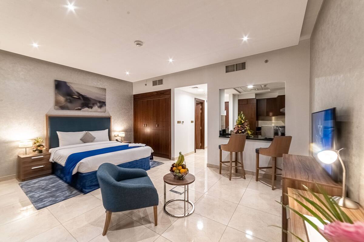 Una habitación de hotel moderna con una cama grande, un escritorio, una silla y una mesita con fruta.