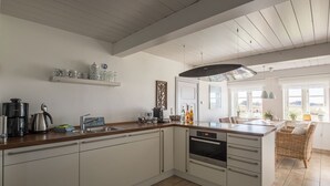 Una cocina con una isla central, muebles blancos, una cafetera, un hervidor y un cartel que dice 'DAS LEBEN NICHT'.